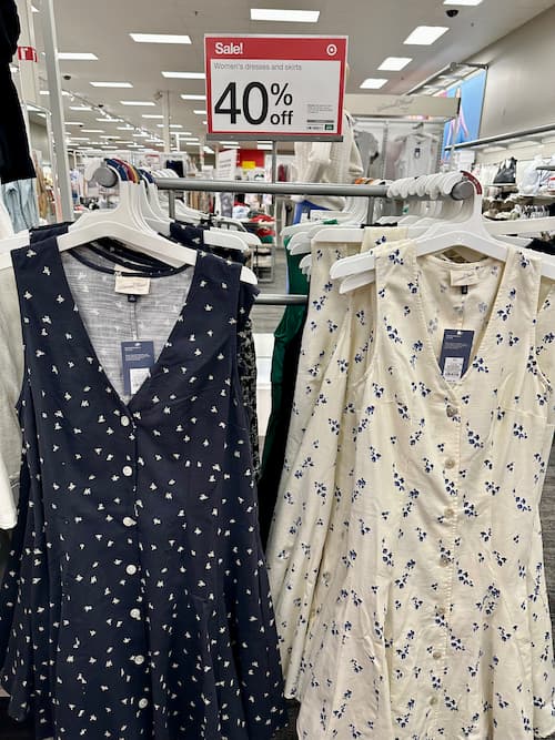 Two floral sundresses on hangers displayed in a Target store under a bold red sale sign reading “40% off Women’s dresses and skirts.” 
